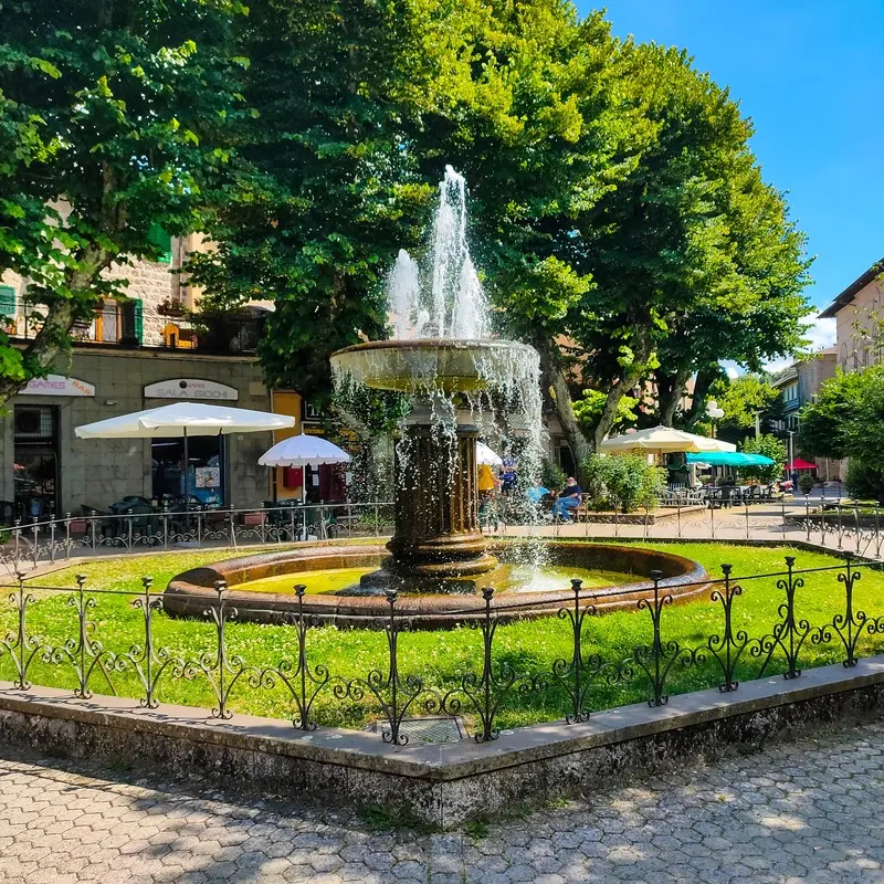 Beautiful fountain in a charming square in Abbadia San Salvatore, Tuscany, surrounded by lush greenery and outdoor cafés.