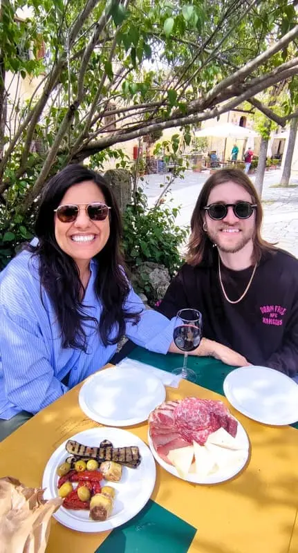 Couple enjoying an outdoor meal in Tuscany: Two people at a table with plates of Italian appetizers, including cheese, salami, and grilled vegetables. Ideal for promoting culinary tours and dining experiences in Tuscany.