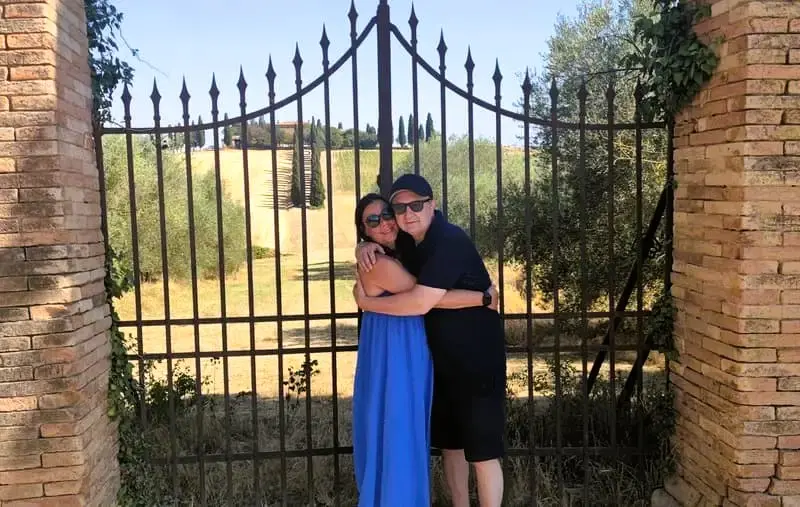 Couple embracing in front of an iron gate in Tuscany: Two people hugging with a scenic Tuscan landscape visible through the gate. Ideal for promoting romantic getaways and scenic tours in Tuscany.