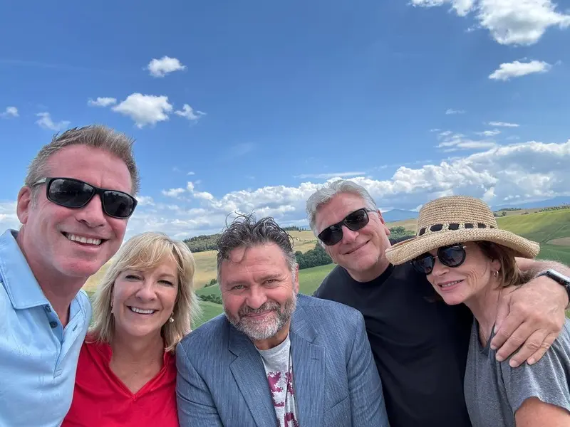 Fabrizio with two couples on a tour in Italy: Fabrizio poses for a selfie with two couples against a backdrop of a scenic landscape with a blue sky and white clouds. Ideal for promoting guided tours and travel experiences in Italy with Fabrizio.