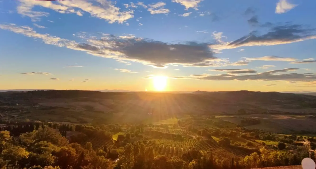 Sunset over the Tuscan hills: A panoramic view of rolling hills and valleys with a bright sun setting against a blue sky with clouds. Ideal for promoting sunset tours and scenic views in Tuscany.