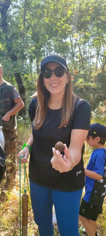 Truffle hunting experience in Italy: Woman holding a freshly found truffle in a wooded area, with other participants in the background. Ideal for promoting truffle hunting tours and culinary adventures in Italy.