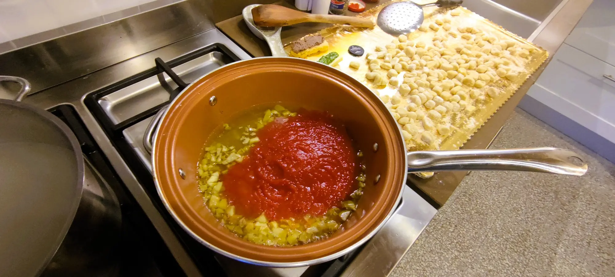 Italian cooking preparation: Chopped garlic and tomato sauce simmering in a pot on a stovetop, with pasta in the background. Ideal for promoting Italian cooking classes and culinary tours in Tuscany.