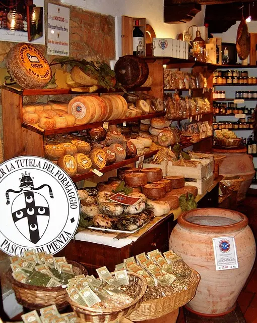 Pecorino di Pienza cheese shop in Tuscany, Italy: Shelves filled with various cheeses, including Pecorino di Pienza, displayed with local products and the 'Tutela del Formaggio' logo. Ideal for promoting food tours and culinary experiences in Tuscany.