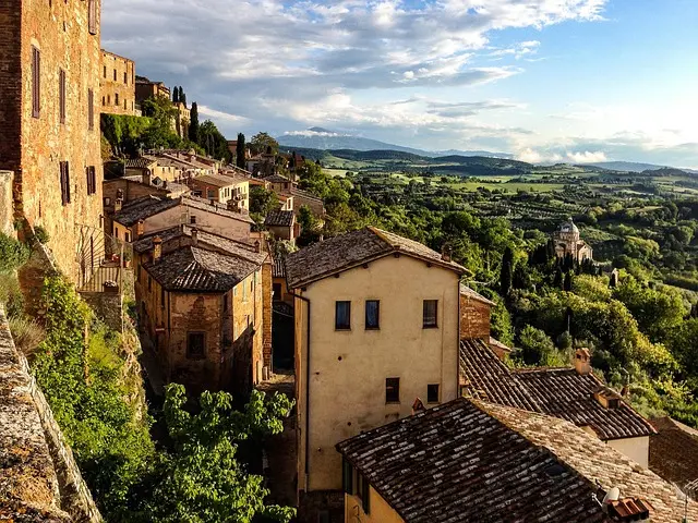 Scenic view of Montepulciano, Tuscany, Italy: Historic buildings with terracotta roofs nestled on a hillside overlooking green valleys and distant mountains. Ideal for promoting Montepulciano tours and Tuscan countryside travel experiences.