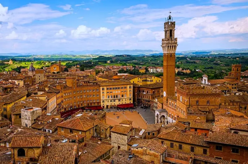 Aerial view of Piazza del Campo, Siena, Italy: A panoramic view of the historic square with the Palazzo Pubblico and Torre del Mangia, surrounded by terracotta rooftops and the Tuscan landscape. Ideal for promoting Siena tours and cultural experiences.
