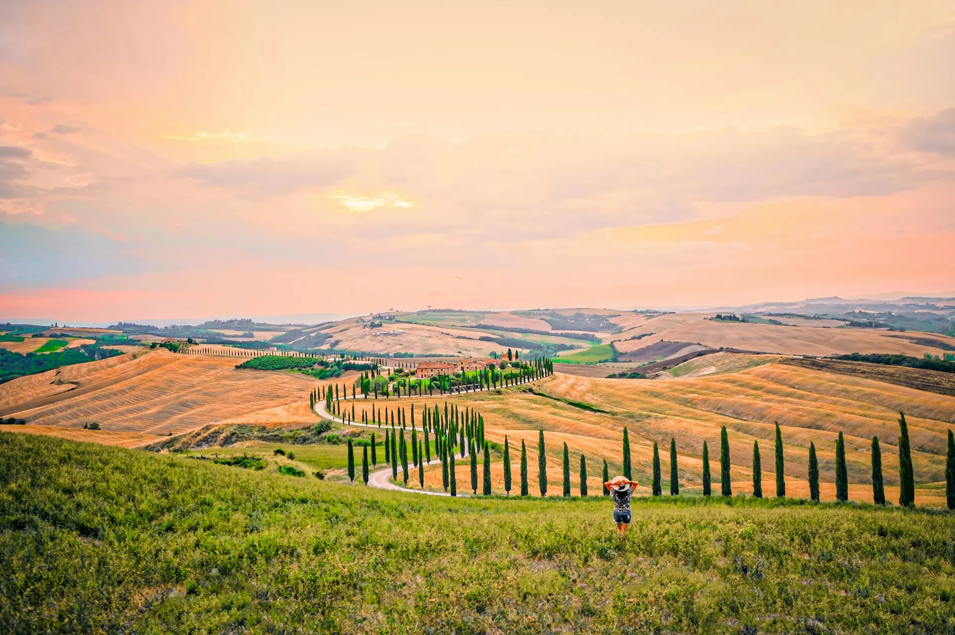 Sun shining over the rolling hills of Tuscany with a winding cypress-lined road leading to a historic villa, showcasing the region’s breathtaking landscape.