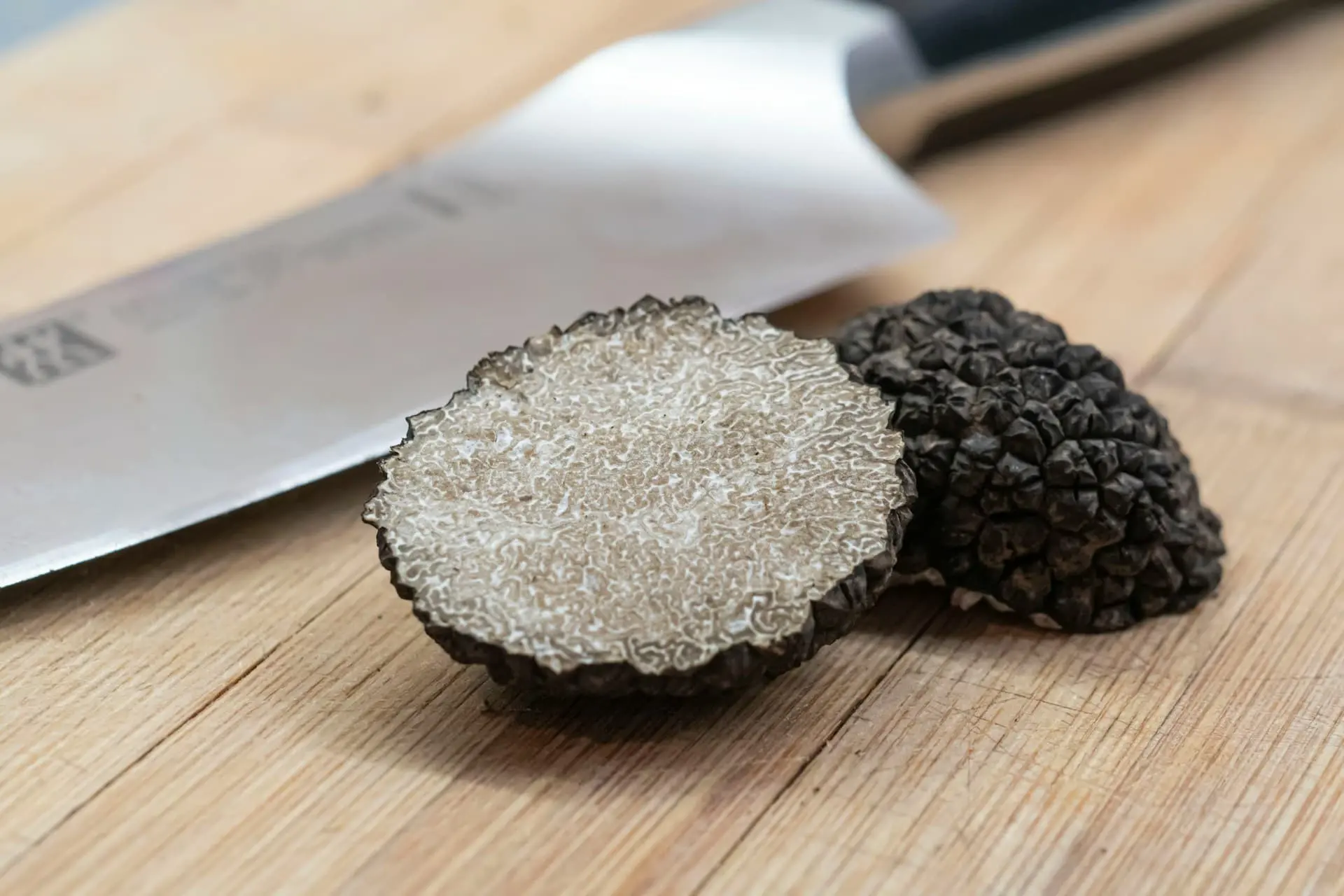 Black truffle close-up: A sliced black truffle on a wooden surface with a knife in the background, showcasing a gourmet ingredient for Italian cuisine. Ideal for promoting truffle tours and culinary experiences in Italy.