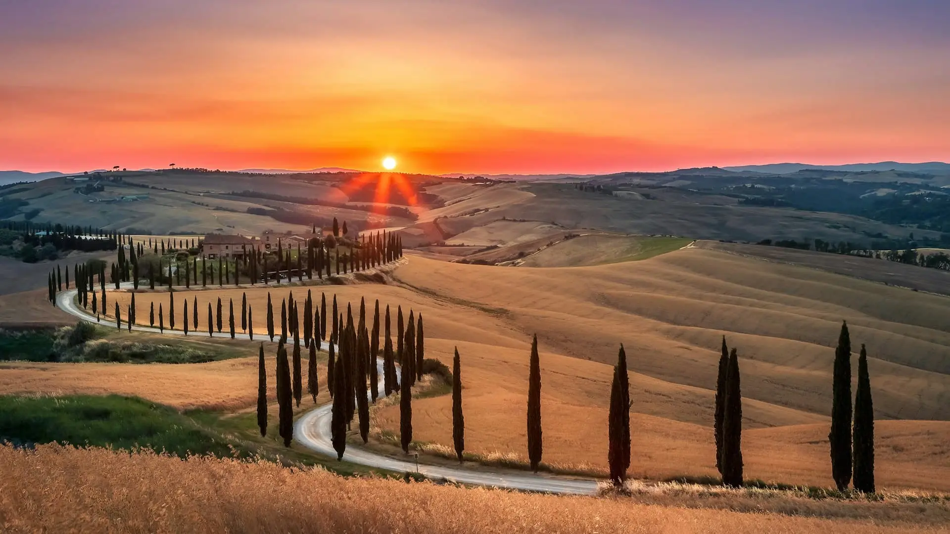 Sunset over the rolling hills of Tuscany with a winding cypress-lined road leading to a historic villa, showcasing the region’s breathtaking landscape.